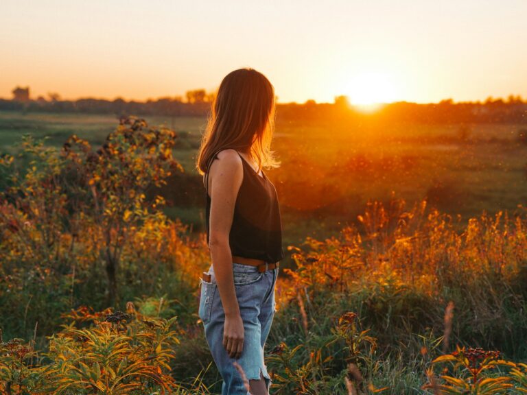 A figure standing quietly in a golden sunlit field at dusk, looking outward with ease