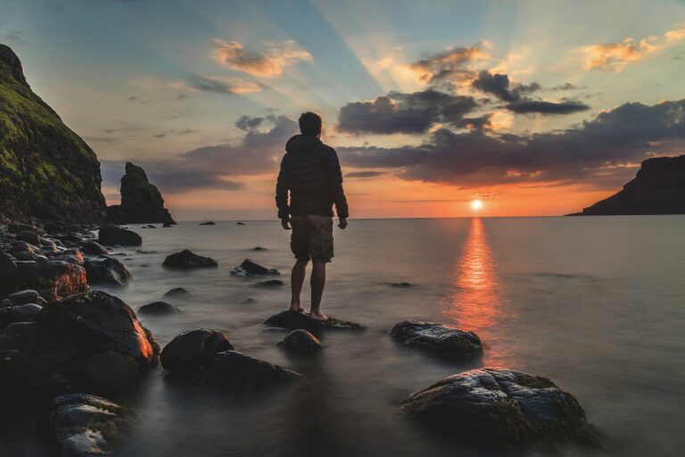 A person standing on rocks at sunset, fully present in the moment, warm golden light on the horizon